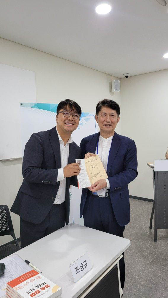 저자 사인회에서 서명한 책을 전달하는 두 사람